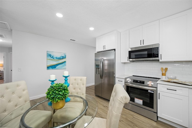 3927 Spence Ave, Tampa, FL 33614 - kitchen featuring appliances with stainless steel finishes, light wood finished floors, backsplash, white cabinetry, and light countertops