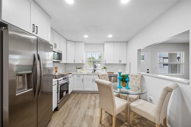 3927 Spence Ave, Tampa, FL 33614 - kitchen featuring stainless steel appliances, a sink, light wood-type flooring, white cabinetry, and tasteful backsplash