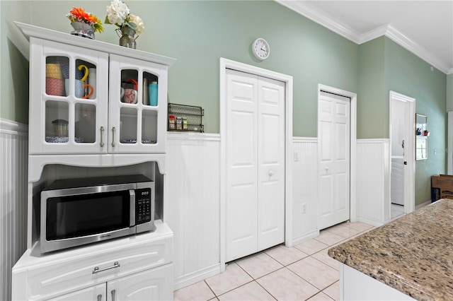 9830 Caribou Trl, Dade City, FL 33525 - kitchen with stainless steel microwave, ornamental molding, light tile patterned floors, a wainscoted wall, and glass insert cabinets