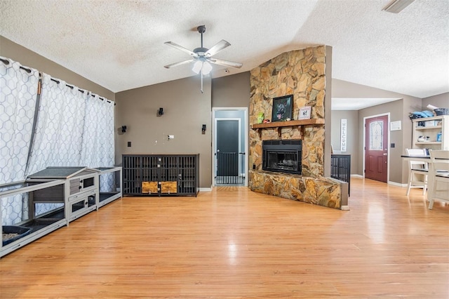 10954 96th St, Largo, FL 33773 - living room featuring vaulted ceiling, a textured ceiling, light wood-style floors, ceiling fan, and a stone fireplace