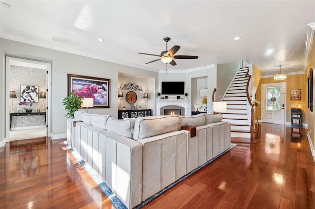 15936 Ternglade Dr, Lithia, FL 33547 - living room featuring stairway, a ceiling fan, dark wood-type flooring, a lit fireplace, and ornamental molding