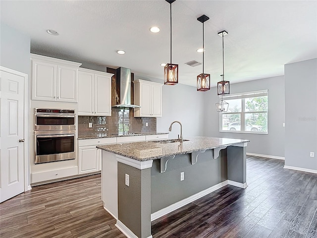 7628 Surf Reed Way, Wesley Chapel, FL 33545 - kitchen with a sink, wall chimney exhaust hood, stainless steel double oven, dark wood-style floors, and a kitchen breakfast bar
