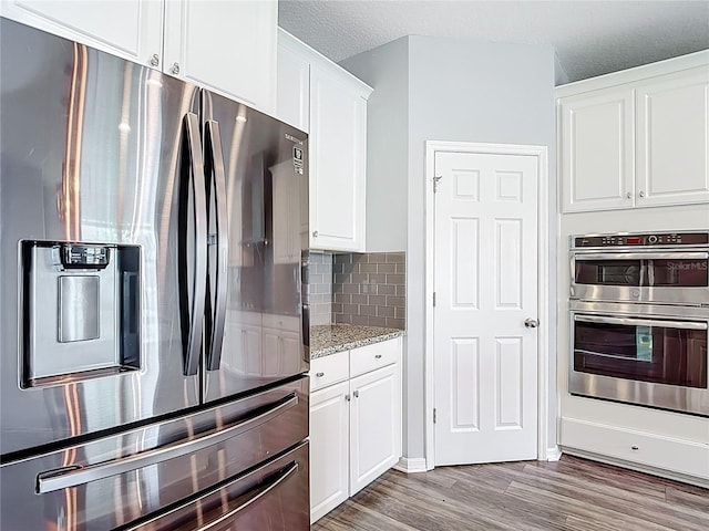 7628 Surf Reed Way, Wesley Chapel, FL 33545 - kitchen with stainless steel appliances, white cabinetry, wood finished floors, tasteful backsplash, and light stone countertops