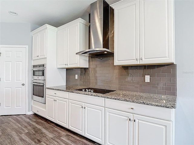 7628 Surf Reed Way, Wesley Chapel, FL 33545 - kitchen featuring wall chimney exhaust hood, black electric stovetop, stainless steel double oven, and dark stone counters