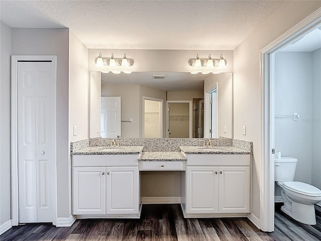 7628 Surf Reed Way, Wesley Chapel, FL 33545 - bathroom featuring wood finished floors, two vanities, baseboards, toilet, and a textured ceiling