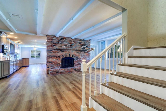 1670 Fox Rd, Clearwater, FL 33764 - unfurnished living room with beam ceiling, a brick fireplace, light wood-style flooring, stairs, and a sink