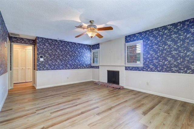 1670 Fox Rd, Clearwater, FL 33764 - unfurnished living room featuring wood finished floors, wallpapered walls, a brick fireplace, ceiling fan, and a wainscoted wall