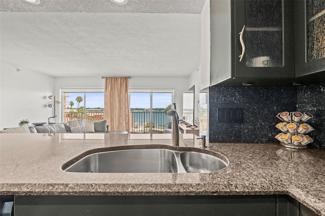 7432 Sunshine Skyway Ln S Unit 402, Saint Petersburg, FL 33711 - kitchen featuring a sink, decorative backsplash, a textured ceiling, open floor plan, and dark stone countertops