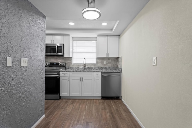 13046 Leverington St, Tampa, FL 33624 - kitchen featuring stainless steel appliances, a sink, dark wood-style flooring, white cabinetry, and a textured wall