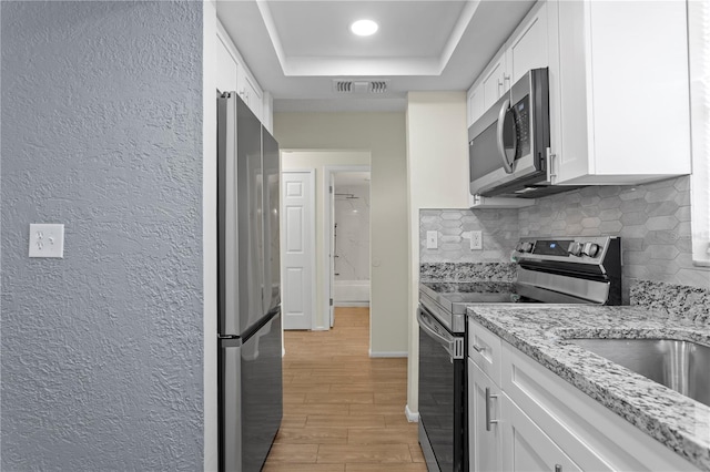13046 Leverington St, Tampa, FL 33624 - kitchen featuring appliances with stainless steel finishes, a textured wall, a raised ceiling, light wood-style floors, and white cabinetry