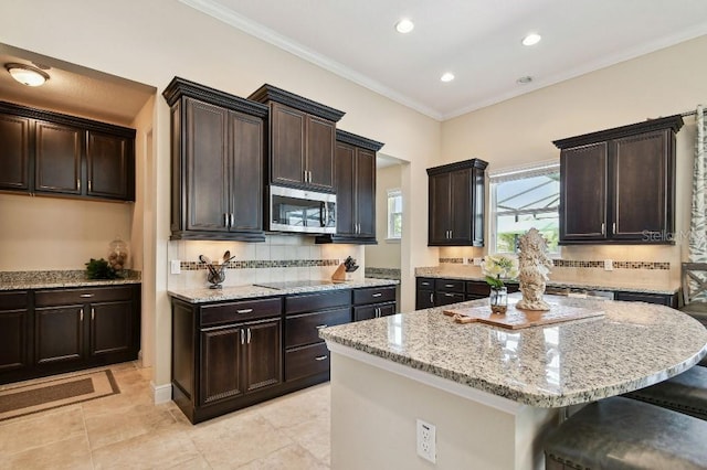 1140 Terralago Way, Kissimmee, FL 34746 - kitchen featuring stainless steel microwave, light stone counters, backsplash, a breakfast bar area, and dark brown cabinets