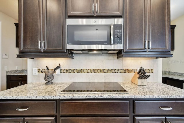 1140 Terralago Way, Kissimmee, FL 34746 - kitchen with stainless steel microwave, black electric cooktop, dark brown cabinetry, backsplash, and light stone counters