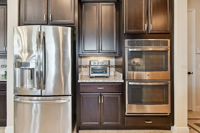 1140 Terralago Way, Kissimmee, FL 34746 - kitchen with appliances with stainless steel finishes, dark brown cabinetry, light stone counters, and baseboards