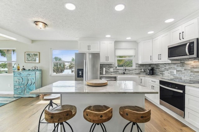 3285 Minnow Creek Dr, Hernando Beach, FL 34607 - kitchen with appliances with stainless steel finishes, a kitchen breakfast bar, tasteful backsplash, light wood-type flooring, and a center island