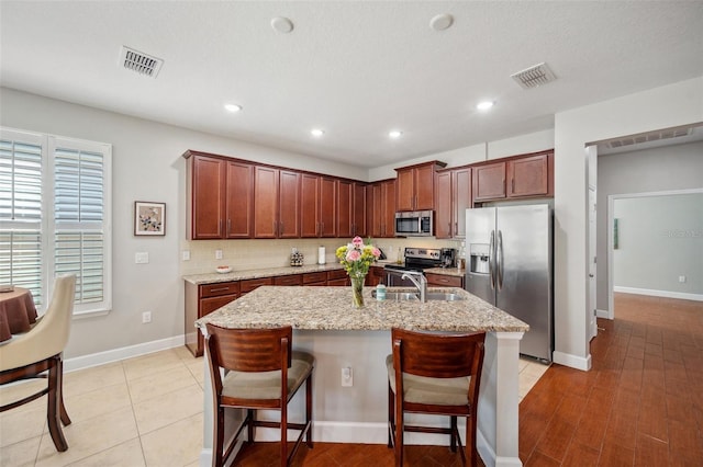 11314 American Holly Dr, Riverview, FL 33578 - kitchen featuring stainless steel appliances, a sink, an island with sink, light stone counters, and a kitchen bar