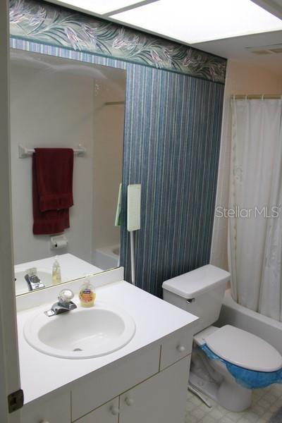 9722 Indian Key Trl Unit 116, Seminole, FL 33776 - bathroom with vanity, toilet, shower / bathtub combination with curtain, and wallpapered walls