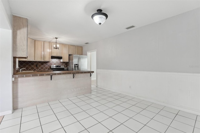 1212 Blake Ave, Auburndale, FL 33823 - kitchen with appliances with stainless steel finishes, under cabinet range hood, a peninsula, light brown cabinetry, and a chandelier