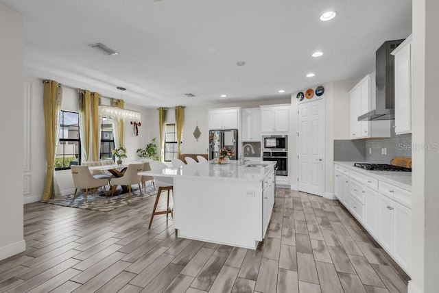 12650 Shetland Walk Dr, Lithia, FL 33547 - kitchen featuring wall chimney range hood, stainless steel appliances, light wood-type flooring, white cabinetry, and decorative backsplash