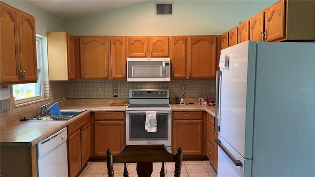 6405 Klaus Ct, Port Charlotte, FL 33981 - kitchen with white appliances, a sink, decorative backsplash, brown cabinetry, and vaulted ceiling