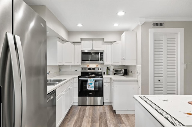 22004 Dupree Dr, Land O Lakes, FL 34639 - kitchen with appliances with stainless steel finishes, a sink, crown molding, light wood finished floors, and white cabinets