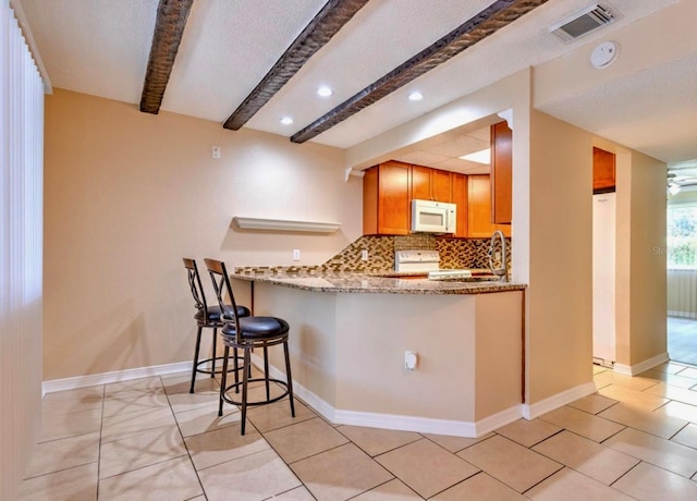 1877 Pine Cone Cir, Clearwater, FL 33760 - kitchen with white microwave, beamed ceiling, stove, tasteful backsplash, and light stone counters