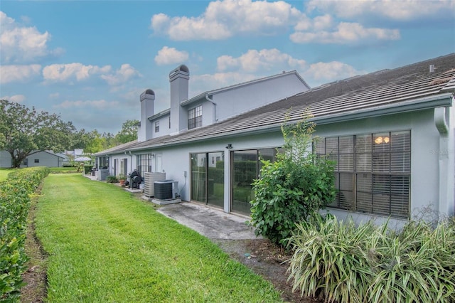4234 Brentwood Park Cir, Tampa, FL 33624 - rear view of property featuring stucco siding, a lawn, a chimney, a tile roof, and central AC unit