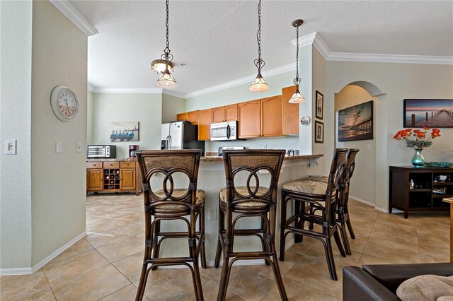 2773 Via Cipriani Unit 1310A, Clearwater, FL 33764 - kitchen with appliances with stainless steel finishes, crown molding, light tile patterned floors, hanging light fixtures, and a kitchen bar