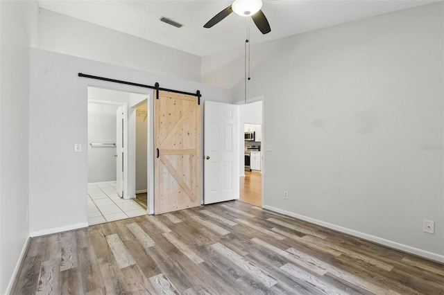 16109 Rambling Vine Dr E, Tampa, FL 33624 - unfurnished bedroom featuring vaulted ceiling, wood finished floors, a barn door, baseboards, and a ceiling fan
