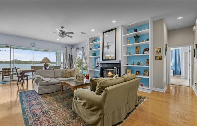 8701 Lake Calm Ln, Odessa, FL 33556 - living room featuring a glass covered fireplace, light wood-style floors, ceiling fan, built in shelves, and baseboards