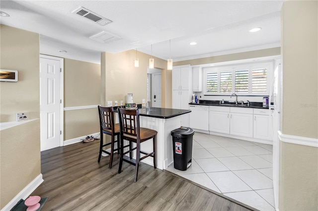 6309 Newtown Cir Unit 9B2, Tampa, FL 33615 - kitchen with dark countertops, a breakfast bar area, white cabinets, light wood-type flooring, and ornamental molding