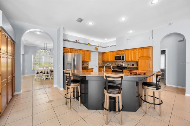 1516 E Lake Woodlands Pkwy, Oldsmar, FL 34677 - kitchen featuring stainless steel appliances, arched walkways, a kitchen bar, light tile patterned flooring, and a spacious island