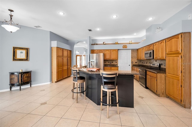 1516 E Lake Woodlands Pkwy, Oldsmar, FL 34677 - kitchen featuring appliances with stainless steel finishes, arched walkways, a breakfast bar area, brown cabinets, and a kitchen island with sink