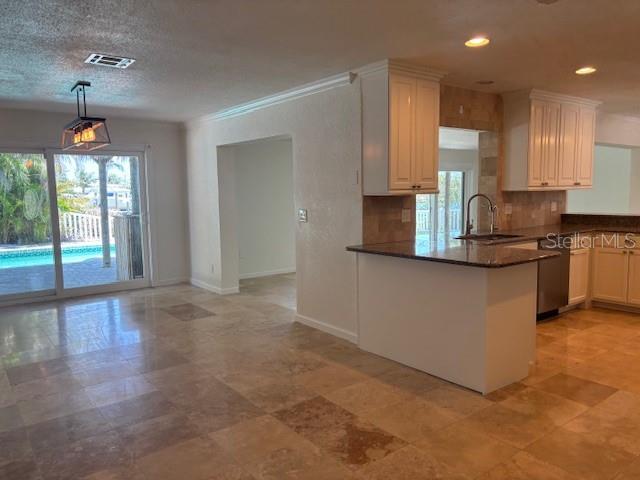 12055 4th St E, Treasure Island, FL 33706 - kitchen featuring dark countertops, a peninsula, tasteful backsplash, dishwasher, and hanging light fixtures