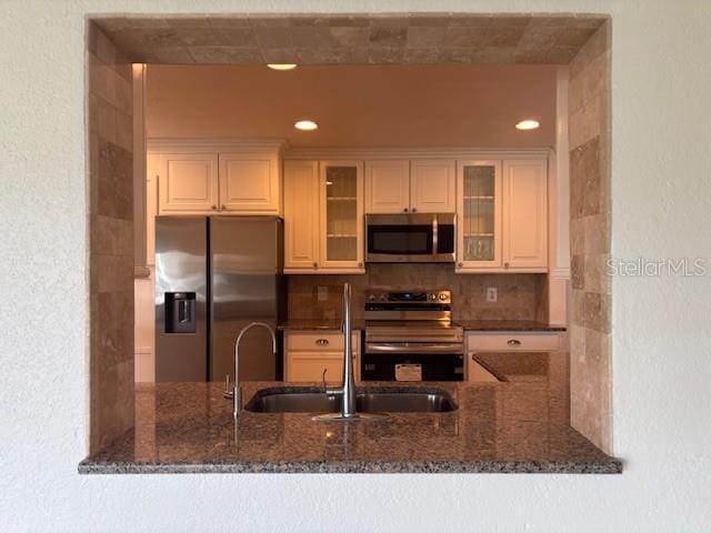12055 4th St E, Treasure Island, FL 33706 - kitchen featuring appliances with stainless steel finishes, a peninsula, dark stone countertops, glass insert cabinets, and recessed lighting