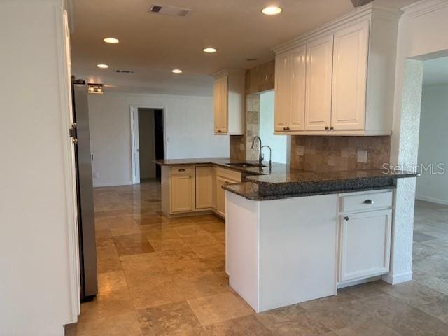 12055 4th St E, Treasure Island, FL 33706 - kitchen with a peninsula, recessed lighting, decorative backsplash, white cabinetry, and freestanding refrigerator