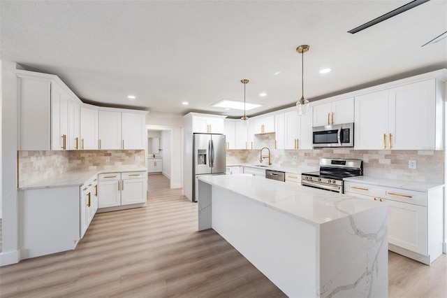 7607 22nd Ave W, Bradenton, FL 34209 - kitchen with stainless steel appliances, a kitchen island, backsplash, white cabinetry, and light wood-type flooring