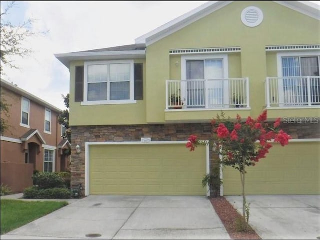 5107 5th Way N, Saint Petersburg, FL 33703 - view of front of home featuring stone siding, a garage, concrete driveway, a balcony, and stucco siding