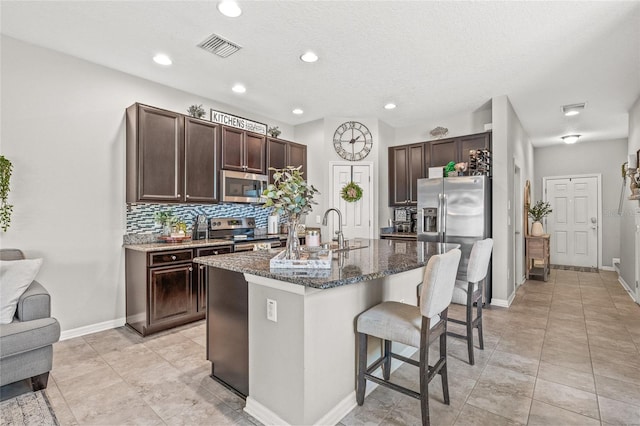 6974 Holly Heath Dr, Riverview, FL 33578 - kitchen featuring stainless steel appliances, a sink, a breakfast bar area, dark brown cabinetry, and dark stone countertops