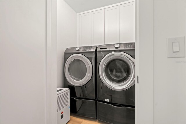 2620 Cove Cay Dr Unit 704, Clearwater, FL 33760 - washroom with washer and clothes dryer, cabinet space, and light wood-type flooring