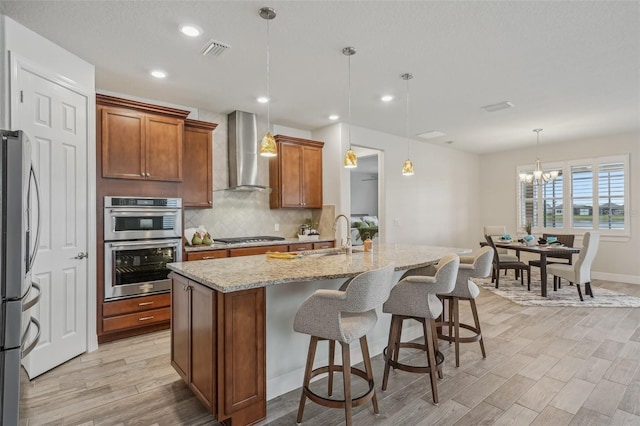 19183 Coastal Shore Ter, Land O Lakes, FL 34638 - kitchen with wall chimney range hood, light wood-style floors, decorative backsplash, light stone countertops, and brown cabinets
