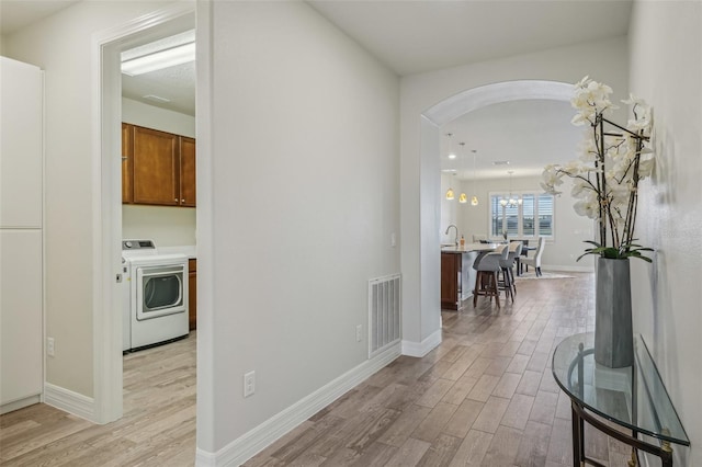 19183 Coastal Shore Ter, Land O Lakes, FL 34638 - hallway featuring washer / clothes dryer, light wood-style floors, arched walkways, baseboards, and a sink