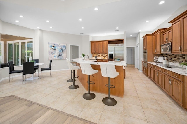 4962 Turtle Creek Trl, Oldsmar, FL 34677 - kitchen featuring appliances with stainless steel finishes, brown cabinets, backsplash, a breakfast bar area, and a kitchen island with sink