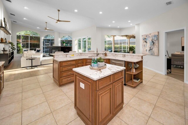 4962 Turtle Creek Trl, Oldsmar, FL 34677 - kitchen featuring a kitchen island with sink, brown cabinets, light tile patterned floors, open floor plan, and light stone counters