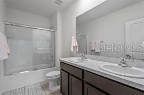 3446 Suncoast Plains Dr, Odessa, FL 33556 - full bath featuring toilet, double vanity, enclosed tub / shower combo, and tile patterned flooring