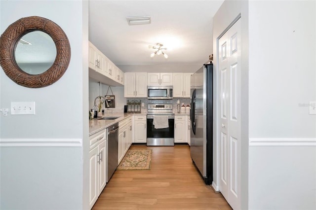 2311 64th Street Ct W, Bradenton, FL 34209 - kitchen with appliances with stainless steel finishes, a sink, white cabinetry, light wood-type flooring, and decorative backsplash