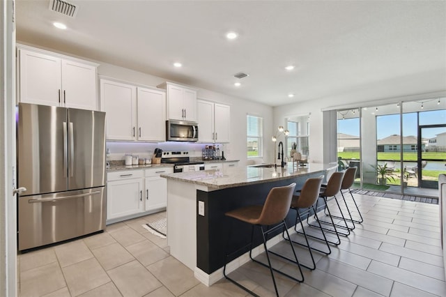 12517 Nantahala Run, Parrish, FL 34219 - kitchen featuring appliances with stainless steel finishes, a center island with sink, white cabinets, light stone countertops, and a breakfast bar