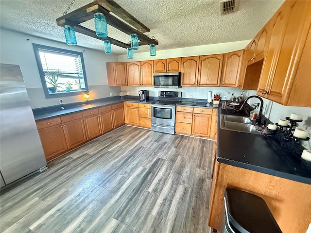 439 Corbett Rd, Lithia, FL 33547 - kitchen with appliances with stainless steel finishes, a sink, a textured ceiling, wood finished floors, and brown cabinets