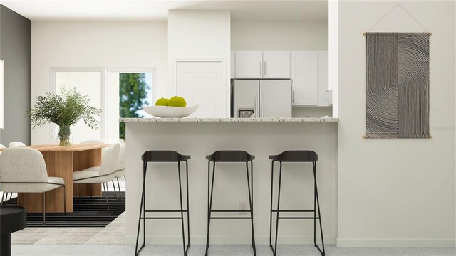 10233 Trumpet Honeysuckle Way, San Antonio, FL 33576 - kitchen with white fridge with ice dispenser, a kitchen bar, white cabinets, baseboards, and a peninsula