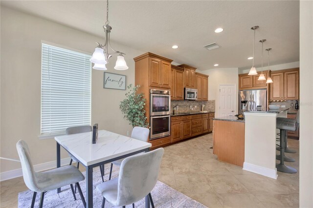 1229 Hillandale Reserve Dr, Tampa, FL 33613 - kitchen featuring stainless steel appliances, tasteful backsplash, brown cabinetry, decorative light fixtures, and recessed lighting