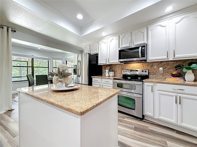 66 Bay Woods Dr, Safety Harbor, FL 34695 - kitchen with stainless steel appliances, white cabinetry, decorative backsplash, a kitchen island, and light wood finished floors